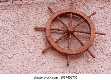 Old Vintage Sailing Steering Wheel From An Old Boat Is Pinned On A Pink Wall With All Its Memories