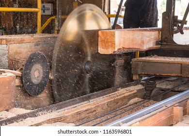 Old Vintage Sawmill with Large Spinning Saw Blade and Raw Lumber being cut and Sawdust flying.