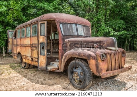 Old vintage school bus abandoned left to decay an empty shell rusting with flat tires and broken windows parked by trees on a sunny day