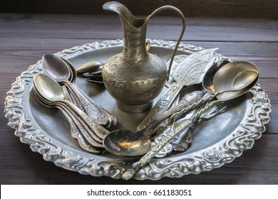 Old vintage silver kitchen equipment utensil tableware silverware with ornament pattern and small eastern jug on a tray on dark table