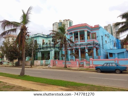 Old vintage Soviet / Russian car parked on dirty street in front of colorful colonial Cuban house with palm trees in poor neighborhood / street in Vedado, Havana, Cuba 