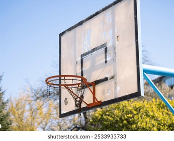 Old and vintage street basketball hoop backboard, worn whit rust chain net. Close up point of view, sunny day blue sky in park whit trees - Powered by Shutterstock