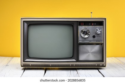 An Old Vintage Television Set From The 1970s Stands On A Wooden Table Against A Yellow Background. Vintage TVs 1980s 1990s 2000s.