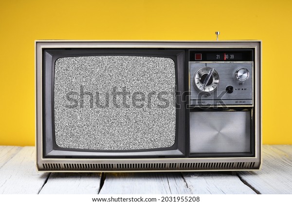 An old vintage TV\
set from the 1970s with interference and noise on the screen stands\
on a wooden table against a yellow background. Vintage TVs 1970s\
1980s 1990s 2000s. 