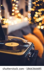 Old Vintage Vinyl Record Player In A Cozy Home, Livingroom With Lots Of Warm Fairy Lights And Orange Pillows, Couch, Family Time Concept, Music, Christmas And New Year Songs, Music Listening