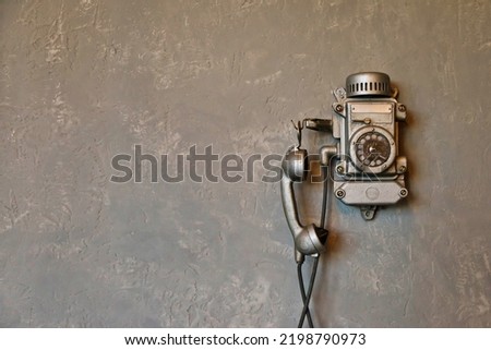 Old vintage wired telephone for communication on textured gray wall. Antique phone from past for design backgrounds. History of telephone in world. Concept of communications and telegraph. Copy space