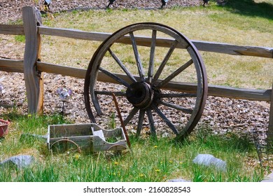 Old vintage wooden cart wheel with small toy coach wagon farm, garden or front yard decoration in grass by fence countryside photo. Exterior landscape design. 