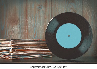 Old vinyl plate and a stack of discs against a wooden wall background.Stylized photo.