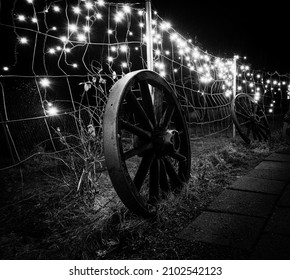 An old wagon wheel leaned against a fence at night under sparkling lights