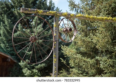 Old Wagon Wheels And Rims, Made Of Rusted Metal, Hanging On The Moss Covered Wood Entrance Arch Gate On A Rural Ranch 