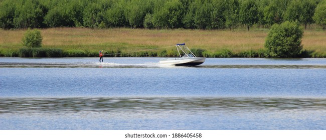 Old wakeboard boat towing a wakeboerder rider on green shore background at Sunny summer day, outdoor activities on the river, water skiing, wakeboard, watersports lifestyle - Powered by Shutterstock