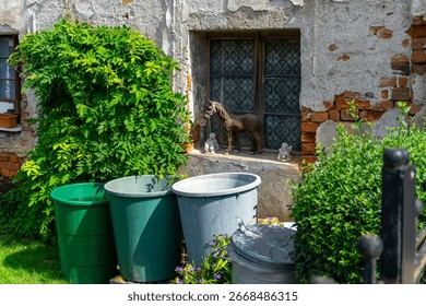 Old wall of a decayed building with window, decorated with horse figurine and small statues, next to plastic water containers.