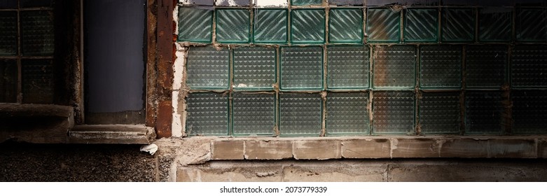 Old Wall With A Window Made Of Square Gray And Glass Tiles. Rough Ribbed Surface Of Dirty Green Glass. Vintage Texture For Background And Design.