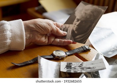 An old watch next to an old woman's hand. Next to old photos. Memories, nostalgia, time concept