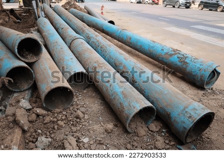 Old water pipes on the side of the road. Pile of deteriorated and broken blue PVC plumbing pipes in urban area on paved road background in construction site with copy space and selective focus.