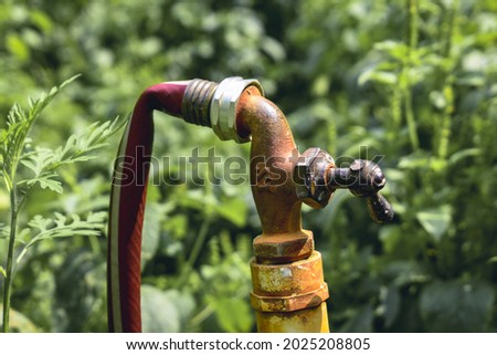 A old water spigot with a broken handle with a red garden hose attached to it- a kink in a old water hose that is attached to an old garden faucet- An outside water spigot- a broken well water spigot