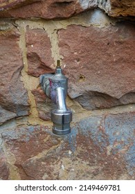 Old Water Tap Protrudes From Rustic Sandstone Wall As Part Of Garden Irrigation System