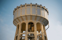 An Old Water Tower Made Of Cement And Metal Spiral Staircase Is An Elevated Structure Supporting A Water Tank Constructed By The Influence European Architecture. Large Water Tank. Selective Focus.
