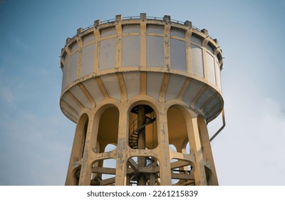 An old water tower made of cement and metal spiral staircase is an elevated structure supporting a water tank constructed by The influence European architecture. Large water tank. Selective focus.
