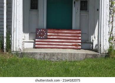 Old And Weathered Colonial Flag Wooden Block Sits On Front Porch