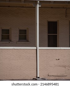 Old Weathered Exterior Brick Wall Of Front Porch Of Building Or Home With Vertical Water Drainage Post Dividing One Window On Right And Two Small Windows On Left Of Home Composition And Symmetry 