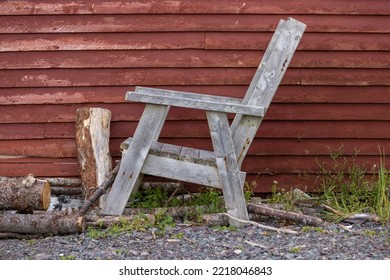 An Old, Weathered, Homemade Chair Sits In Front Of A Wood Shed In Rural Newfoundland.  