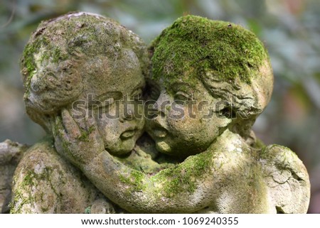 An old, weathered and moss covered sandstone culpture of two angels that comfort each other.