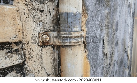 Old weathered pipe attached to a damaged wall with a rusty metal clamp bracket