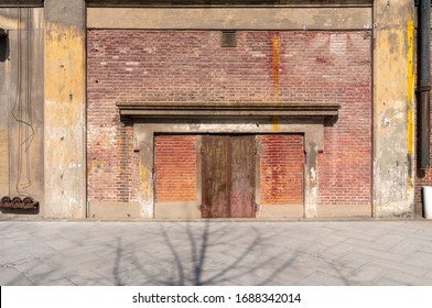 Old weathered rusty factory gate and the dated brown brick wall in the sunlight