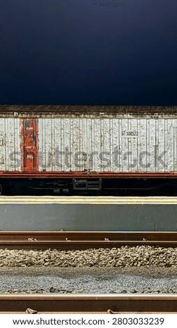 Old weathered white cargo train boxcar on a railway track at night with dark sky background, industrial aesthetic.