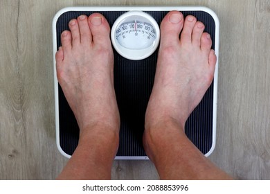 Old weight scale stood on my adult male seeing point of view of scale standing on. Adult white male weighing his self on an old worn black and white weight scale on a wood grain design vinyl floor.