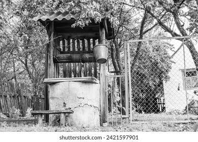Old well with iron bucket on long forged chain for clean drinking water, photography consisting of old rounded well with roof, clear water in big bucket, spring water at aluminum bucket from old well