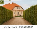 An old well maintained house with a clay tile roof. Country house with gravel driveway and green hedge.