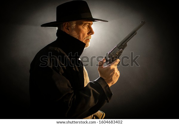 Old west gun fighter holding\
his pistol ready for a fight. Photo lit from behind with smoke\
added