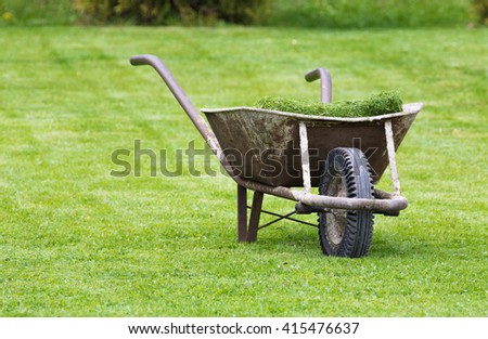 Old wheelbarrow on a lawn with fresh grass clippings in summer