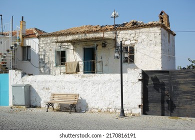 An Old White Farmhouse Exterior. Ancient Rustic House On The Street With A Broken Damaged Roof, Tiny Square Windows And Brick Walls. Open Windows In Thick Stone Wall Of An Weathered Antique Building