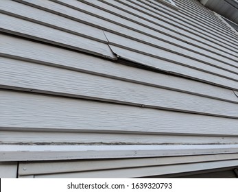 Old white metal siding on the back of a house coming loose near a window and needing repairs or replacement and renovations