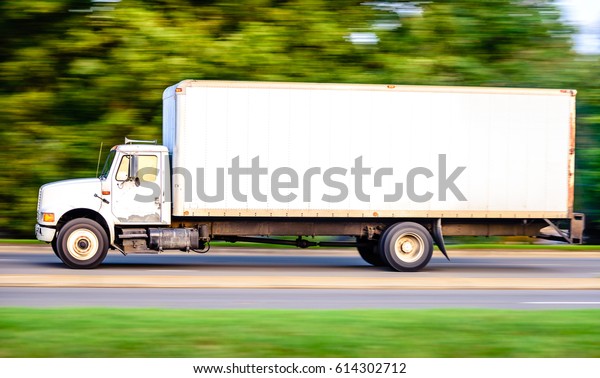 An\
old white truck is running down the highway captured early morning\
during summer season. This image was captured using panning\
technique to blur the background and emphasize\
motion.