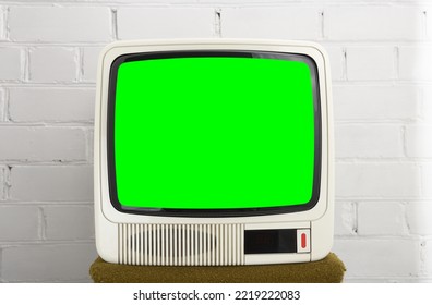 An Old White TV From The 90s With A Green Screen Against A Brick Wall. Retro Technology Concept.