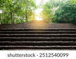 Old wide red stone staircase among green trees. Stairway step through a historical park with beautiful sunlight at above. Old stony steps in Prasat Hin Khao Phanom Rung Park, Thailand.