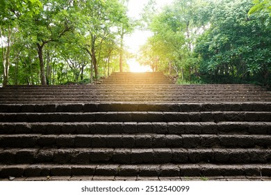 Old wide red stone staircase among green trees. Stairway step through a historical park with beautiful sunlight at above. Old stony steps in Prasat Hin Khao Phanom Rung Park, Thailand. - Powered by Shutterstock