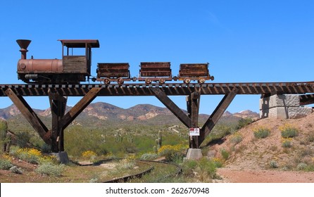 Old Wild West train with mining carts passing over an old wooden bridge with mountains, cactus and wild flowers in background