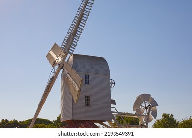 Old Windmill In Landscape View Showing Staitionary Sails And Wind Vain Just Above Tree Height. 