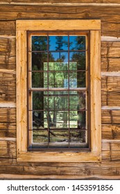 An old window on a rustic cabin with highly textured wood planks surrounding it.