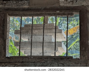 Old Window with Wire Mesh Screen and Rusty Frame in Old Concrete Wall