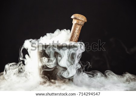 Old witcher cauldron illed with magic potion and deep smoke around at black background.