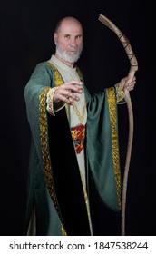 old wizard dressed in a dark green robe with gold embroidery. He holds his magic staff in his hands.