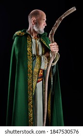 old wizard dressed in a green cloak with a hood. He holds his magic staff in his hands.