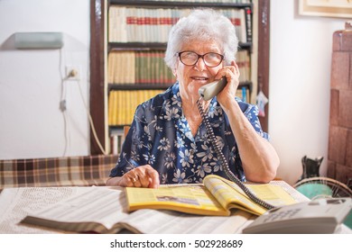 Old Woman With Address Book Talking On Telephone At Home.