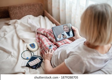 Alte Frau im Bett, die einen Bildschirm mit Laptop anschaut und sich zu Hause mit einem Arzt berät, Telehealth-Dienste während des Absperrens, Ferngespräche, moderne medizinische Anwendungen